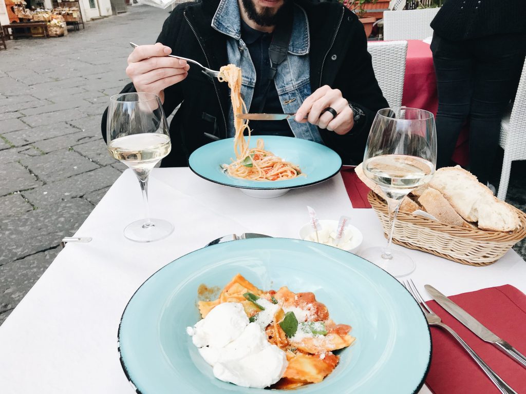 Dinner table with a plate of ravioli, 2 wine glasses and basket of fresh bread and Drew in the middle of eating his spaghetti plate. At Royal in Piazza di Amalfi